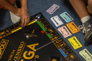 Hráči sa zabávajú pri hre Monopoly na komunitnom podujatí v kultúrno-komunitnom dobrovoľníckom priestore Hory Doly v Liptovskom Mikuláši, kde sa spája zábava a socializácia v rámci miestnej komunity.